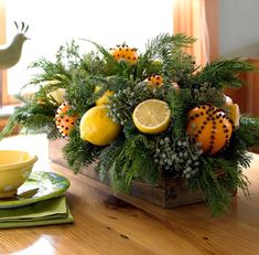 an arrangement of fruit and greenery is displayed on a table in front of a window