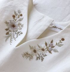 two white linens with embroidered flowers and leaves on them, sitting next to each other