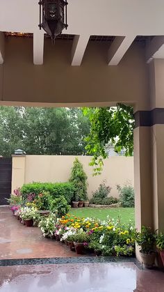 a clock hanging from the side of a building next to a lush green park filled with flowers