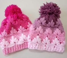 two crocheted hats with pom - poms on top of each other