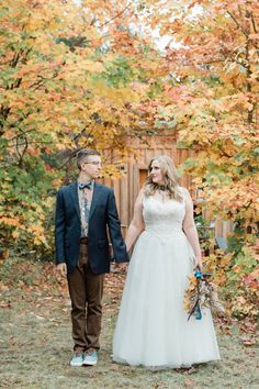 a bride and groom holding hands in front of colorful trees