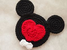 a crocheted mickey mouse head with a heart on it's forehead, sitting on a white surface