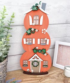 an orange house shaped like a stack of books on a wooden table next to a potted plant