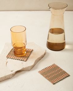 a pitcher and glass on a table with coasters next to eachother,