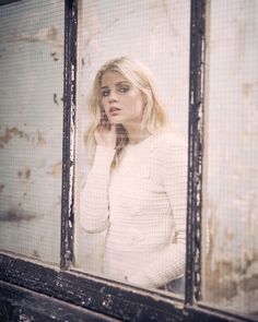 a woman standing in front of a window with her hand on her face and looking at the camera