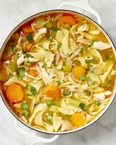 a pot filled with chicken noodle soup on top of a white marble countertop