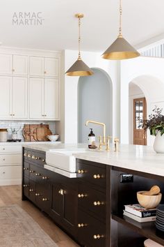 a large kitchen with white cabinets and gold hardware on the counter tops, along with two hanging lights