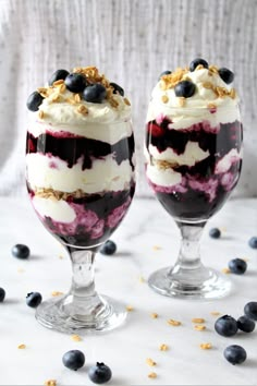 two desserts with blueberries and yogurt in them on a white table