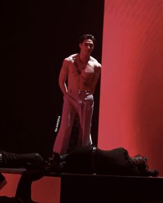 a shirtless man standing on top of a bed in front of a red wall