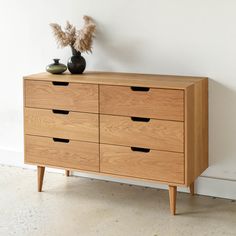 a wooden dresser with four drawers and two vases sitting on it's side