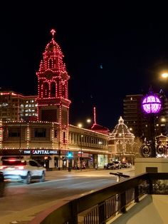 a city street at night with christmas lights on buildings and cars driving down the road