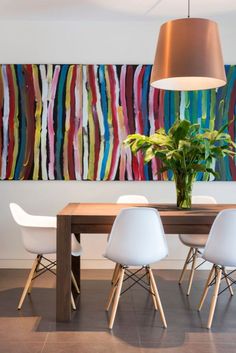 a dining room table with white chairs and a large painting on the wall behind it