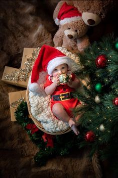 a baby dressed as santa claus is sitting next to a teddy bear and christmas tree