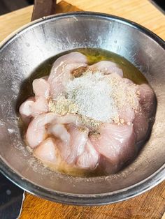 raw chicken in a metal bowl with seasoning and salt on the top, sitting on a wooden table