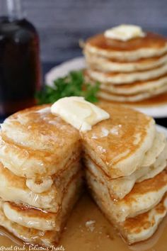 stack of pancakes with syrup and butter on plate next to glass of syrup in background