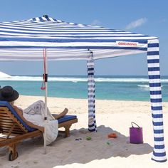 a person sitting on a beach under a blue and white striped tent with the ocean in the background