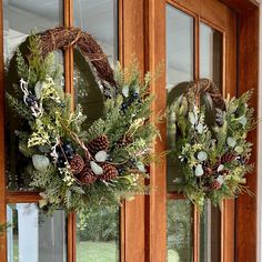 two wreaths on the front door of a house with pine cones and greenery