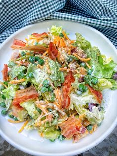 a white plate topped with a salad covered in lettuce and carrots on top of a checkered table cloth