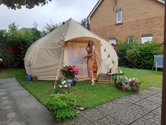 a woman standing in a tent next to some flowers and potted plants on the lawn