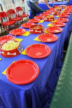 the table is set up with red plates and bowls of food on blue cloths