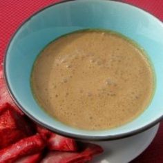 a white bowl filled with brown liquid next to sliced strawberries on a red table