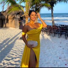 a woman in a yellow dress on the beach with palm trees and chairs behind her