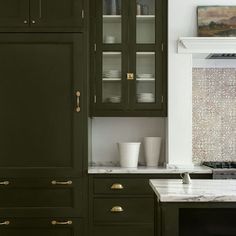 a kitchen with dark green cabinets and marble counter tops, along with brass pulls on the cabinet doors