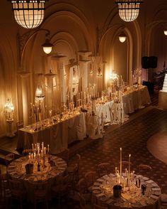 a room filled with lots of tables covered in white tablecloths and lit candles