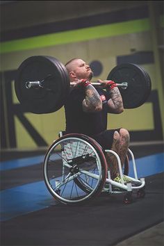 a man in a wheel chair holding two barbells up to his face as he squats down