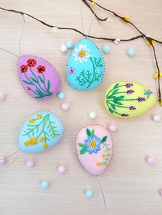 four decorated eggs sitting on top of a wooden table next to some twigs and flowers