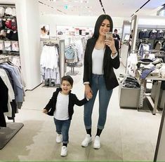 a woman holding the hand of a small child in a clothing store with clothes on racks