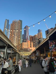 many people are walking around in an outdoor shopping area with lights strung over the buildings