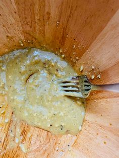 a wooden bowl filled with yellow sauce and a fork in the center, on top of a table