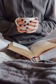 a woman is holding a cup and reading a book