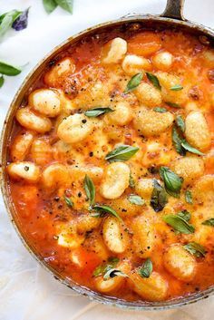 a pot filled with pasta and sauce on top of a white tablecloth next to green leaves