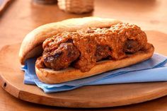 a meatball sandwich on a wooden plate with blue napkins next to some bread