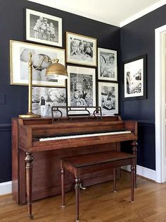 an old piano is in front of several framed pictures on the wall, along with a lamp