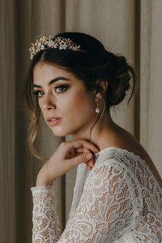 a woman wearing a white lace top with a gold head piece on her head and earrings