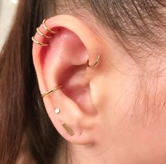 a woman wearing three gold ear cuffs with two small piercings on her left ear