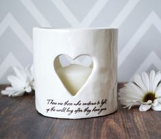 a white coffee mug with a heart cut out on it and some daisies in the background