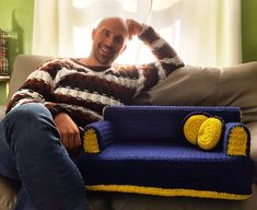 a man sitting on top of a couch next to a blue and yellow sofa cushion