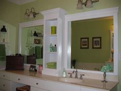 a bathroom with green walls, white cabinets and a large mirror on the wall above the sink