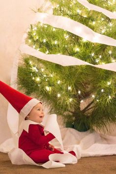 an elf is sitting in front of a christmas tree