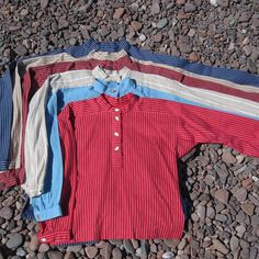 three men's shirts laying on the ground next to some rocks and gravel,