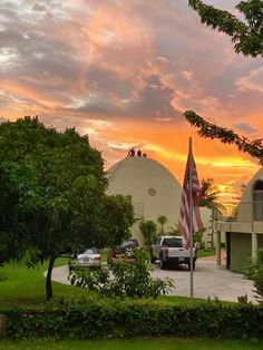 the sun is setting behind two domes in an area with trees, bushes and cars