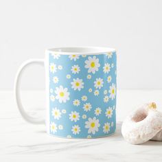 a blue mug with white flowers and a donut next to it on a marble surface