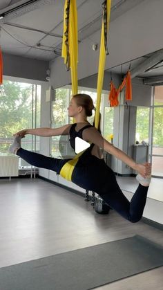 a woman is doing aerial yoga exercises in an empty room with yellow ribbons hanging from the ceiling