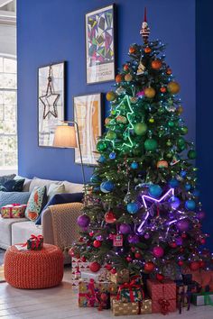 a brightly lit christmas tree stands in the corner of a living room with blue walls