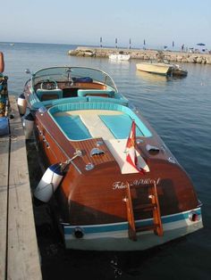 a boat docked at a pier with people standing on the dock and another boat in the water