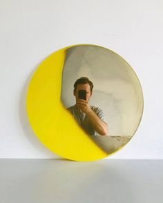 a man taking a selfie in front of a yellow circular mirror on a white wall